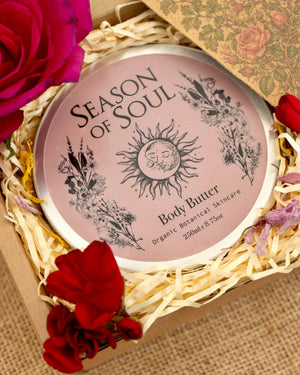 Body butter container with 'Season of Soul' branding surrounded by red flowers on a textured surface.