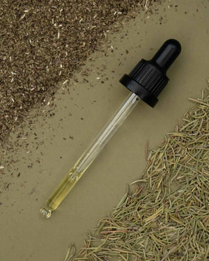 Dropper with yellow liquid on a bed of dried herbs and soil